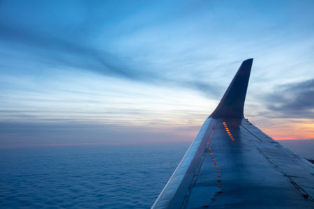 Evening view from the airplane window. The sun has set behind the horizon. Solid clouds are visible under the wingの写真素材