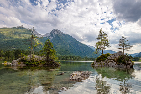 Summer Austria. Clouds over a mountain forest lake. Picturesque stone islands in the foreground