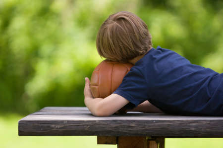 A 4 years old boy in a navy t-shirt with a brown ball in a park. Waiting for a gameの写真素材