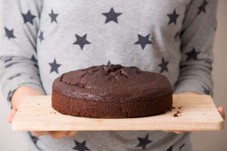 Homemade fresh chocolate birthday cake in the hands of a woman. A nice cake for a party. Grey...