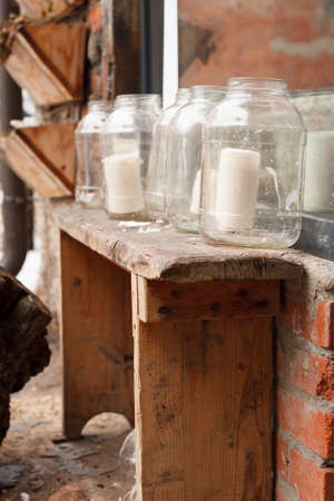 White big candles in glass jars on a narrow retro wooden table outdoors. Simple creative ideas for...