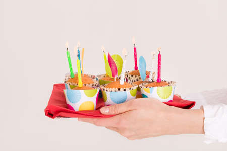 Woman's hands holding a bright tray with muffins and birthday candles. Homemade sweet present for a child's party. Celebration of a birthday.の写真素材