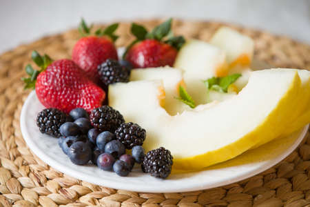 Cut melon and berries. Fruit salad of strawberries, blueberries, melon, mint and blackberries. Diet salad on the white plate - breakfast, weight loss concept. closeup. Healthy snack.の写真素材