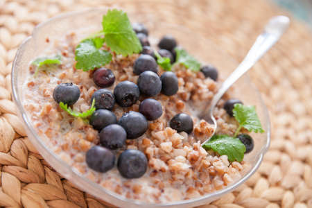 Vegan buckwheat porridge topped with organic blueberries and fresh mint in a glass plate on a straw table mat. Healthy breakfastの写真素材