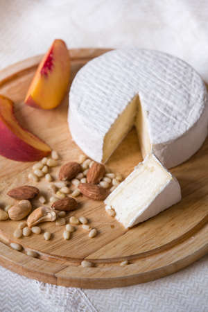 White delicious homemade camambert cheese on a wooden plate served with almonds, cashew, pine nuts and peach. Dessert for a family dinner. Brie.の写真素材