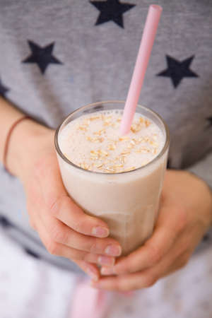 Young woman with a big glass of healthy smoothie served with a straw and oats. Hands holding milkshake. Stars background. Dairy snack or breakfast.の写真素材