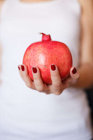 Young woman in a white t-shirt holding a big organic pomegranate in her hand. Healthy lifestyle and nutrition.の写真素材