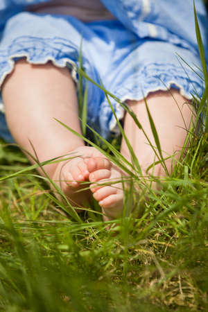 Feet of a small baby on the green grass. Sunny day. Cute child sitting on the ground. Barefoot of a infant.の写真素材