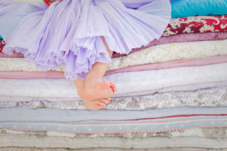 Decorations for fairy tale Princess and the Pea. Little girl with bare feet sitting on the pile of blankets and mattresses. Child in a lilac fluffy skirt at the party. Girl's birthday.の写真素材