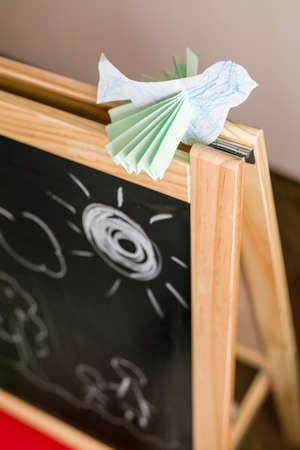 Paper bird on the chalk board in the kid's room. Origami bird made by a child. Bird decoration for child's room. Children drawings on the chalkboard.の写真素材