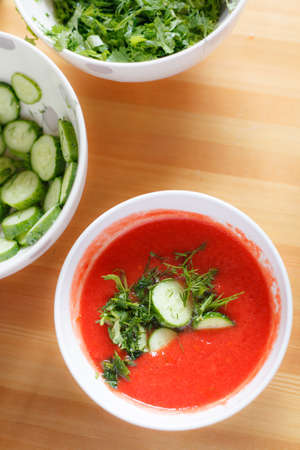 Delicious tomato soup with aromatic spices and organic cucumbers in a white bowl on a wooden table. Healthy luch. Home made food.の写真素材