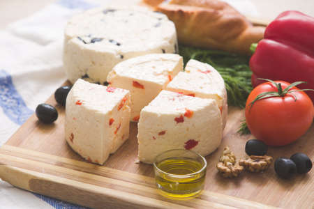 Variety of home made cheese and paprica and herbs, olive oil, olives and bread on a wooden board. brined curd white cheese with vegetables on the tableの写真素材