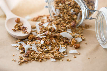 Glass jar of homemade organic granola with coconut and pecans on the baking paper background. Delicious breakfast cereal. Healthy muesli.の写真素材