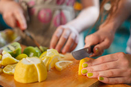 Children cooking at the kitchen. Hands cutting fresh organic lemons on the wooden table. Fruit...