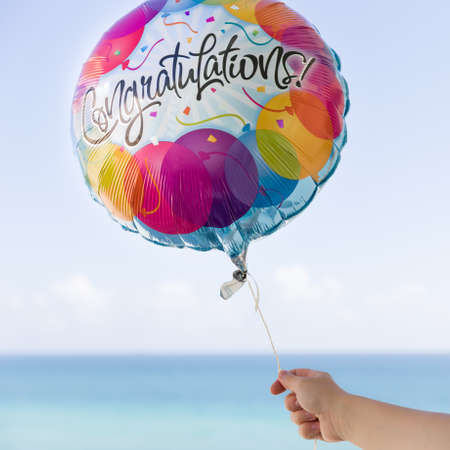 Woman's hand holding colorful baloon on the blue sky background. Congratulation baloon in the air....