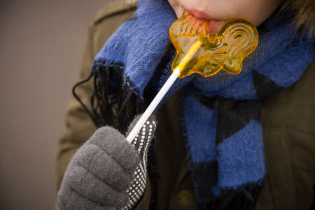 Small kid in warm clothes and nice blue scarf with a big yellow lollipop. Easter celebration. Child...