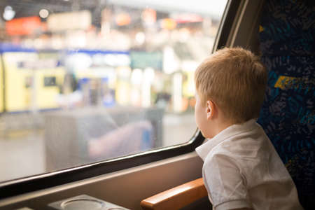 Cute little kid boy in a white t-shirt looking at the city out of the train window.  Child...