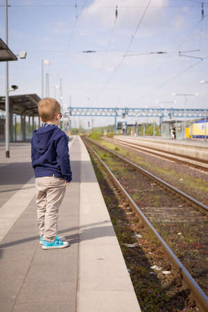 Adorable kid boy waiting for a train at the railway station in a sunny day. Child ready for...