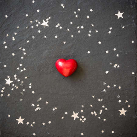 Small red heart on the black background with silver stars. Hearts and stars on a black board....
