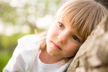 Portrait of adorable blond kid boy looking into the distance and thinking. Serious child dreaming while sitting outdoors.の写真素材