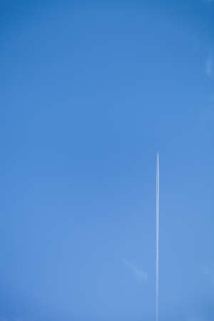 Airplane in blue sky with Vapor Trail. Condensation trail of plane in the sky. Vertical image.の写真素材