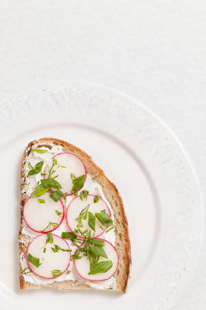Top view on wholegrain sandwich with organic radish and cream cheese on white plate and white background. Healthy food for breakfast or snack. Vegetarian.の写真素材