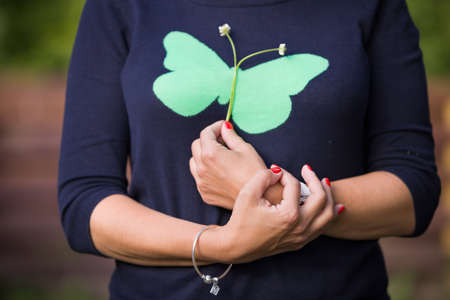 Closeup of young woman in blue sweater with green butterfly holding flowers in her hands. Summer. Outdoor. Girl's hands with flowers.の写真素材