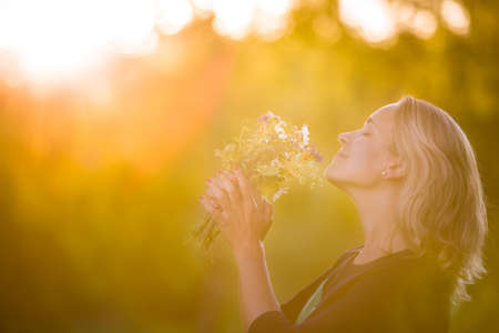 Portrait of beautiful young woman standing on a summer meadow with bunch of wild flowers in her...