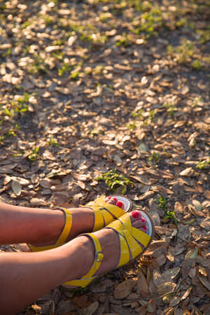 Closeup of woman's feet in bright yellow sandals on the ground. Sunny summer day outdoors. woman walking in the park.の写真素材
