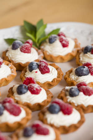 Closeup of delicious homemade cupcakes with vanilla cheese cream and organic blueberries and raspberries on the top served with fresh mint. Healthy dessert for celebration or party.の写真素材