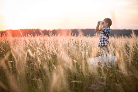 Boy seaman floats on a sailing boat in the field at sunset on a warm evening summer. Dreams of travel! Child floats on a handmade boat against the backdrop of a sunset.の写真素材