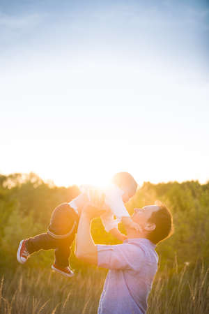 Happy father with his adorable toddler boy son on sunset. Father holding cute baby in the sky on sunny day. Family having fun and enjoying day in the park. Fatherhood, childhood and lifestyle conceptの写真素材