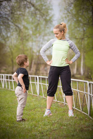 Happy son and mother are doing exercises in the summer park. on the stadium, outdoor. Sport activities with children. Healthy lifestyle. Fitness exercises. Young mother and son are stretching togetherの写真素材