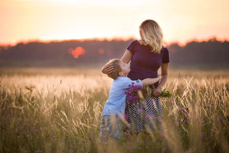 Cute kid boy hugging his mother on a summer meadow on beautiful summer sunset. Happy family together. Mum and child. Motherhood and childhood. Family walking in the field. Outdoors.の写真素材