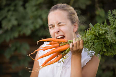 Cheerful young woman with bunch of organic carrots in a vegetable garden. Happy girl holding bunch of fresh carrots. Healthy food. Healthy lifestyle concept.3の写真素材