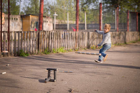 kid boy playing skittles in the street. Russian game skittles. Wooden skittles. Outdoor activites with children. Child playing in the sun.の写真素材