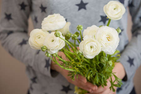 Closeup of woman's hands golding a bunch of beautiful white ranunculus. Grild with bouquet of...
