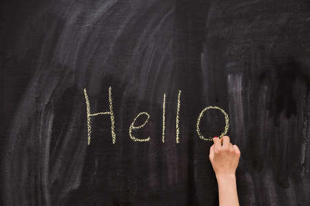 Closeup of child's hand writing Hello word with chalk on the backboard in school class. Education,...