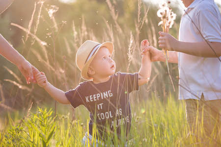 Portrait of cute little toddler boy in a straw hat holding his mother's  and brother's hands. Adorable child walking with his mom and sibling in the park on a sunny summer day. Family on sunset.の写真素材