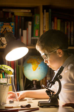 Cute elementary school boy looking into microscope at his desk at home. Young scientist making experiments in his home laboratory. Indoors. Child and science.の写真素材
