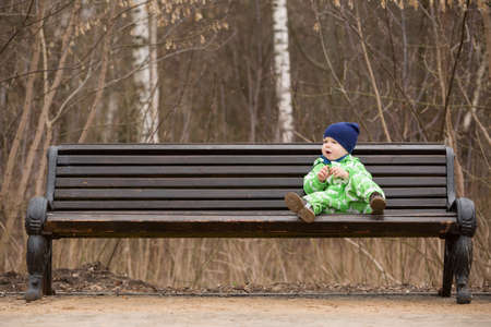 Adorable little toddler boy sitting on a big bench in the park. outdoor walks with children. Child on the park bench.の写真素材