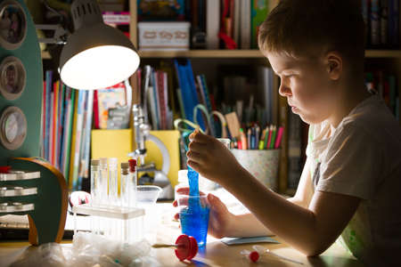 Cute elementary school boy looking into microscope at his desk at home. Young scientist making experiments in his home laboratory. Indoors. Child and science.の写真素材