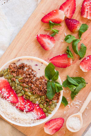 Breakfast berry smoothie bowl topped with strawberry, pumpkin seeds, coconut, muesli and fresh mint. Strawberry banana smoothie bowl. healthy breakfast or snack, wooden tableware.の写真素材