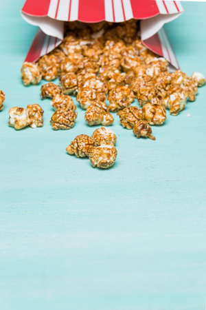 Popcorn on turquoise background. Caramel pocorm in the red and white cup. Cinema. Movie time.