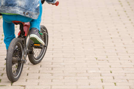 Back view on a kid boy riding on a small bicycle in the park. Child on the bike on asphalt road. Children activities outdoors.の写真素材