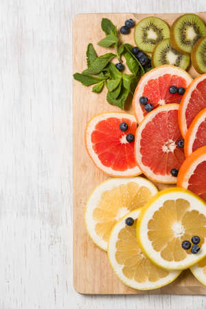 Top view on cut red and yellow grapefruit with mint. Fresh organic citrus, kiwi and blueberry on white wooden background. Healthy snack or fruit dessert.の写真素材