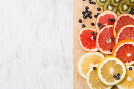 Top view on cut red and yellow grapefruit. Fresh organic citrus, kiwi and blueberry on white wooden background. Healthy snack or fruit dessert.の写真素材