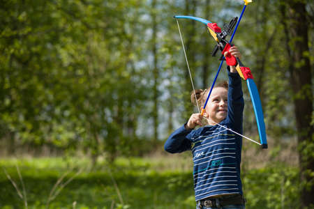 Cute girl archer with bow shooting in sunny summer day. little girl shoots bow in the park....