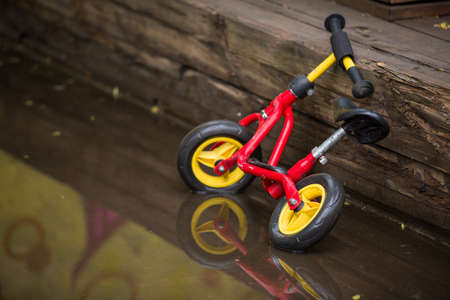 Bright chidren's bicycle standing in a puddle after the rain. Child's bicycle in a big puddle with graffiti wall reflection. Fun after rain. Outdoor activities for children.の写真素材