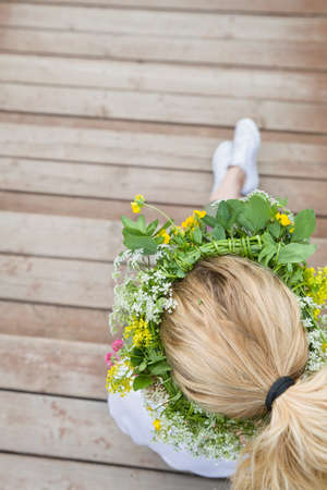 Top view on blond woman's head with wild flowers wreath. Girl with flowers sitting on wooden bridge outdoors. Countryside life. Summer and lifestyle concept.の写真素材
